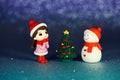 Small table figurines of a girl, a snowman and a Christmas tree on a shiny paper background