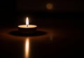 A small tealight candle emits a warm flame, casting a subtle glow on a dark surface. The reflection Royalty Free Stock Photo
