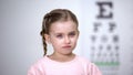 Small tearful girl looking into camera, afraid to wear glasses vision correction