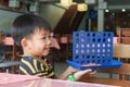 Small Thai boy invites a cafe visitor to play the Connect Four board game