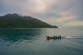 Small Thai traditional boat sailing on clean ocean with lush mountain in soft blue cloudy sky background. tropical country Royalty Free Stock Photo