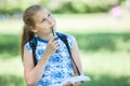 Small thoughtful girl standing in park with sketchbook and pencil in hands, copy space