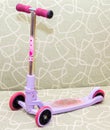Small three-wheeled children pink scooter on couch Royalty Free Stock Photo
