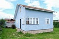 Small tiny wooden frame house painted in blue and white windows and door as a country residence in sunny summer day