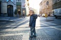 A small toddler boy standing by a road outdoors in city at sunset, looking back. Royalty Free Stock Photo