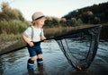 A small toddler boy standing in water and holding a net by a lake, fishing.