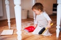 A small toddler girl with brush and dustpan sweeping floor in the kitchen at home.