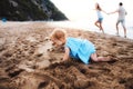 A small toddler girl playing in sand on beach on summer holiday.