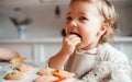 A small toddler girl sitting at the table, decorating cakes at home.