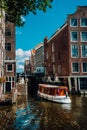 Small Tourist boat floating picturesque dutch channel passing traditional brick houses. Colorful cityscape in Amsterdam Royalty Free Stock Photo