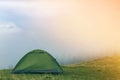 Small tourist tent on grassy mountain hill on fogy tree tops and clear blue sky before sunrise copy space background. Summer Royalty Free Stock Photo