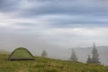 Small tourist tent on grassy mountain hill. Summer camping in mountains at dawn. Tourism concept Royalty Free Stock Photo