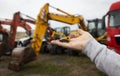 small toy excavator on a man's palm, in the background are real large construction excavators