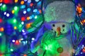 Small toy snowman on colorful Christmas lights background Royalty Free Stock Photo