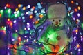 Small toy snowman on colorful Christmas lights background Royalty Free Stock Photo