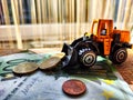 A small toy tractor or excavator on a bundle of money. The concept of the high cost of technology. The possibility of Royalty Free Stock Photo