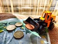 A small toy tractor or excavator on a bundle of money. The concept of the high cost of technology. The possibility of Royalty Free Stock Photo