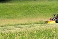 Small tractor with mower in front cutting a steep hillside wildflower meadow in the Alps for hay