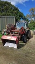 Small tractor with shovel/bucket attachment parked on gravel near a corrugated iron shed Royalty Free Stock Photo