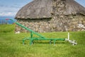 A small traditional hand plough with a thatched house in the background