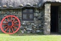 A small traditional stone built cottage with a thatched roof. a collection of metal rims for cart wheels