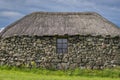 A small traditional stone built cottage with a thatched roof. a collection of metal rims for cart wheels