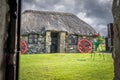 A small traditional stone built cottage with a thatched roof. a collection of metal rims for cart wheels