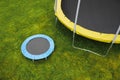 Small trampoline near big one with round mat, size comparison, green lawn background Royalty Free Stock Photo