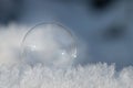 A small transparent soap bubble lies on fresh snow crystals. The background is blue. There is space for text Royalty Free Stock Photo