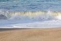 Small transparent wave breaking on sandy shoreline with washback foam