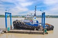 Small towboat moored at river pier on cloudy sky background