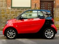 Small two-seater red and black modern compact town car in side view in old urban setting