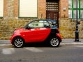 Small two-seater red and black modern compact town car in side view in old urban setting