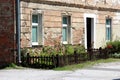 Small urban garden in front of old red brick suburban family house with dilapidated cracked facade surrounded with brown picket Royalty Free Stock Photo