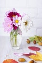 A small vase with autumn flowers is on the table with yellow and red leaves and fallen acorns. Royalty Free Stock Photo