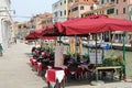 A small Venetian street, restaurant tables by the water canal in Venice, restaurant by the canal bank, umbrellas over restaurant t