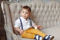 Small very cute boy in yellow pants and suspenders sitting on a