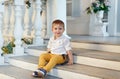 Small very cute, charming boy in yellow trousers sits on the sta