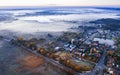 A small villge surrounded by foggy cold fields. Aerial photo from the top above. Road out of city