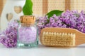 Small vintage glass bottle with purple bath salts epsom salt, foot soak, wooden massage body brush and lilac flowers. Copy space