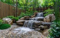 Small waterfall cascades down rock face in lush green backyard with bamboo trees and stone steps. Royalty Free Stock Photo