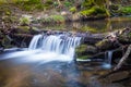 Small waterfall on creek flowing over the rocks and wood