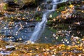 Small waterfall flowing through mossy rocks and fallen colorful autumn leaves Royalty Free Stock Photo