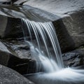A small waterfall flows over smooth dark rocks creating a serene scene Royalty Free Stock Photo