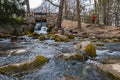 Small waterfall next to path in small Oliwski park with small wooden bridge over it and small pond full of stones