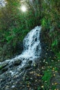 A small waterfall outlet with the sun breakingvthrough the trees lighting the water Royalty Free Stock Photo
