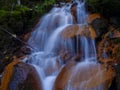 A small waterfall, running water in orange tones. rocks, rocky trees, twigs and moss.