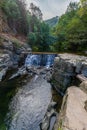 A small waterfall tumbles over dark, layered rocks into a rushing river Royalty Free Stock Photo