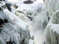 Small waterfalls cascading into narrow river with banks covered in snow and icicle