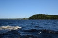 Small waves in the blue Ladoga Lake. A small chapel on the horizon. Clear sky on a summer day and green forest on the coastline